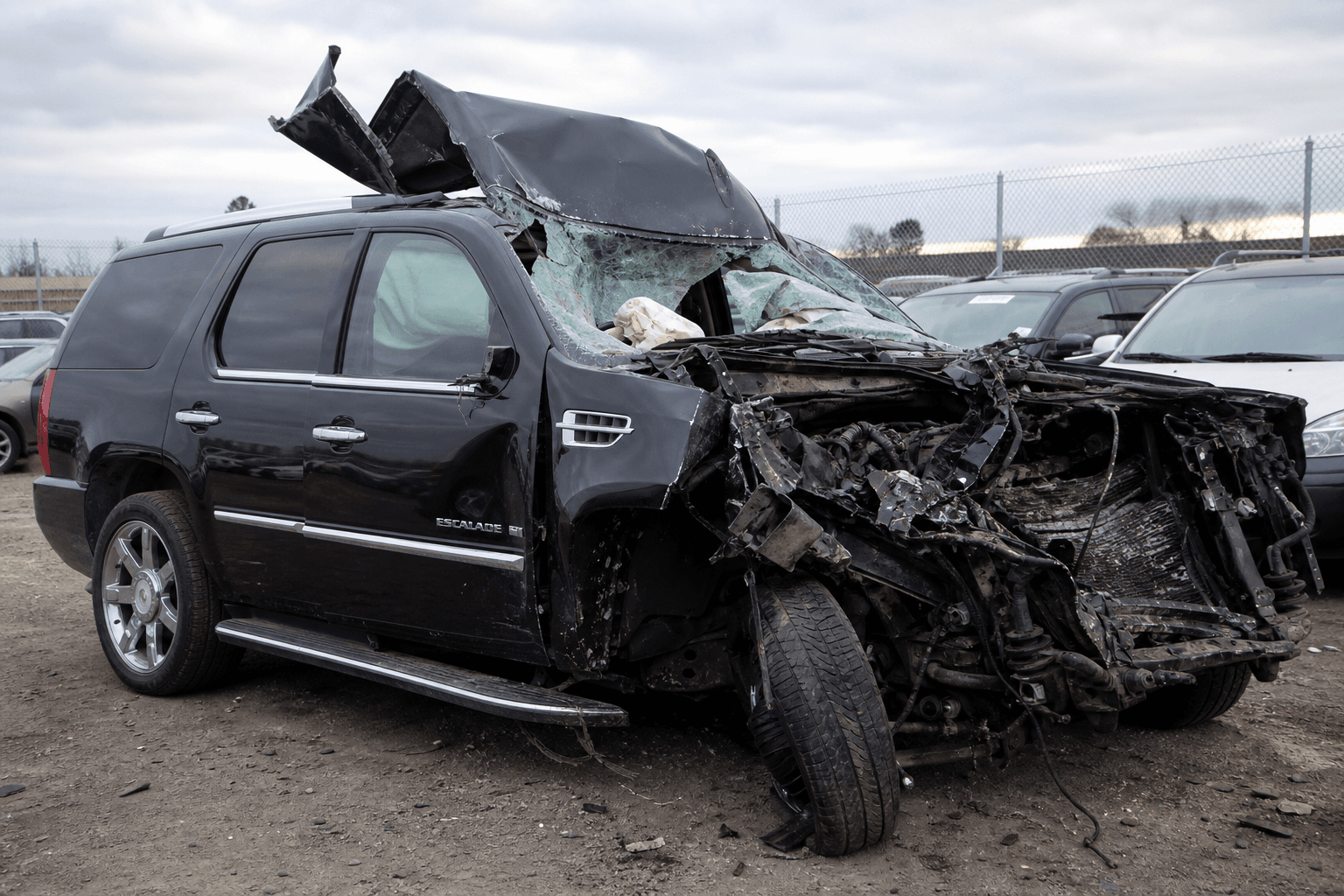 A black 2007 Cadillac Escalade AWD with significant front-end and side-panel damage from a high-impact collision, photographed in a tow yard at dusk.