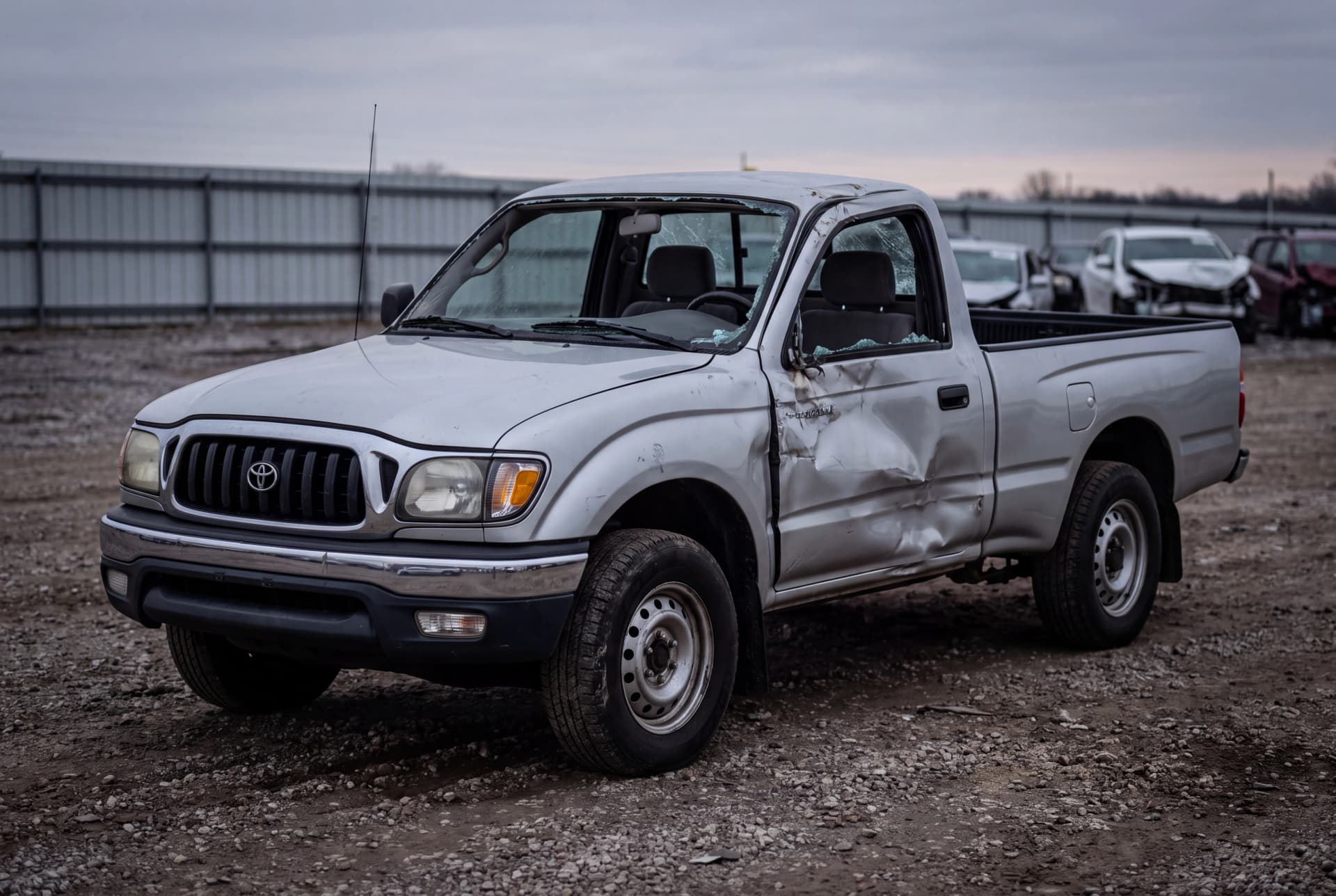 A totaled Silver 2003 Toyota Tacoma Base after a passenger-side collision