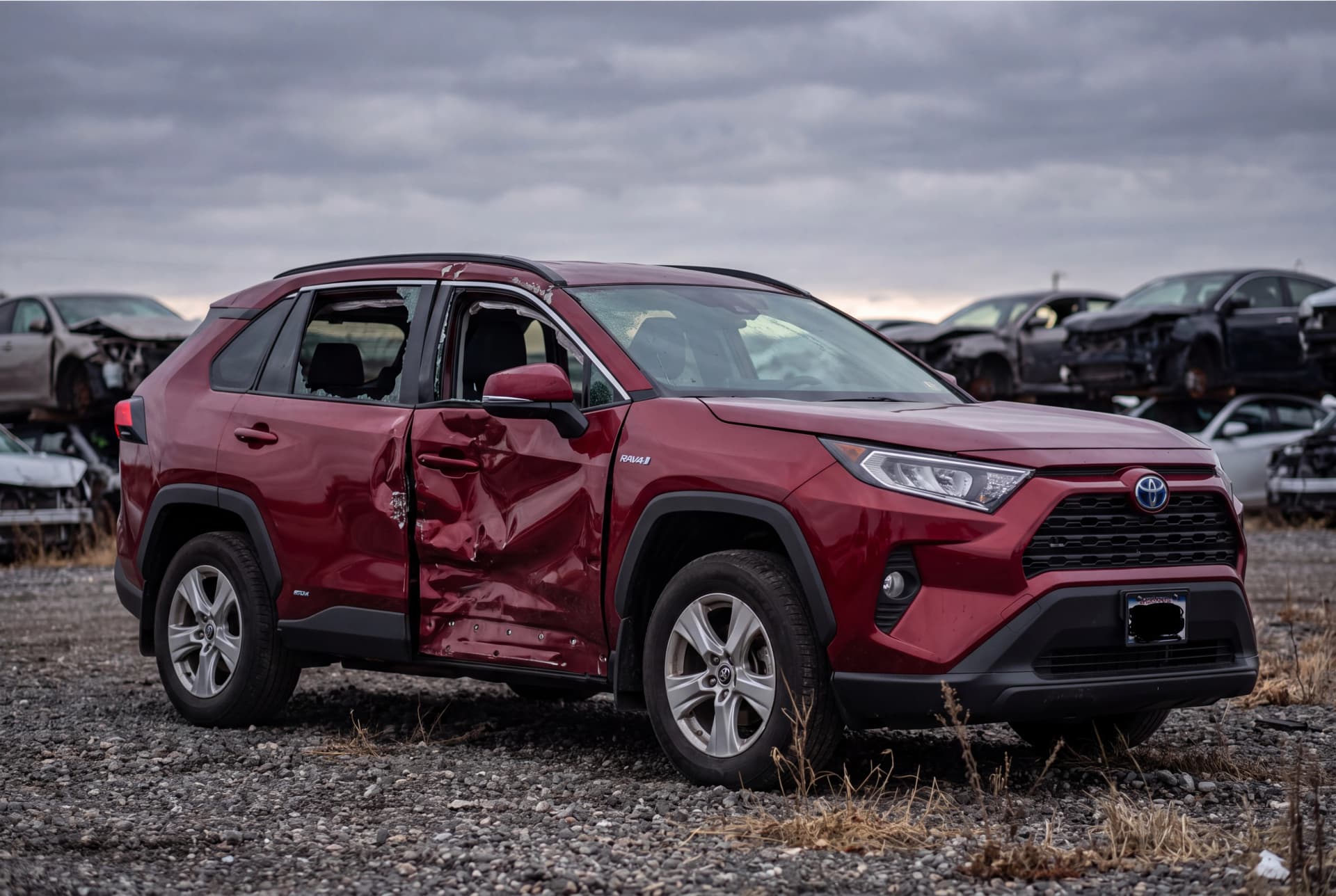 A totaled Ruby Flare Pearl 2021 Toyota RAV4 LE HV after a driver-side collision